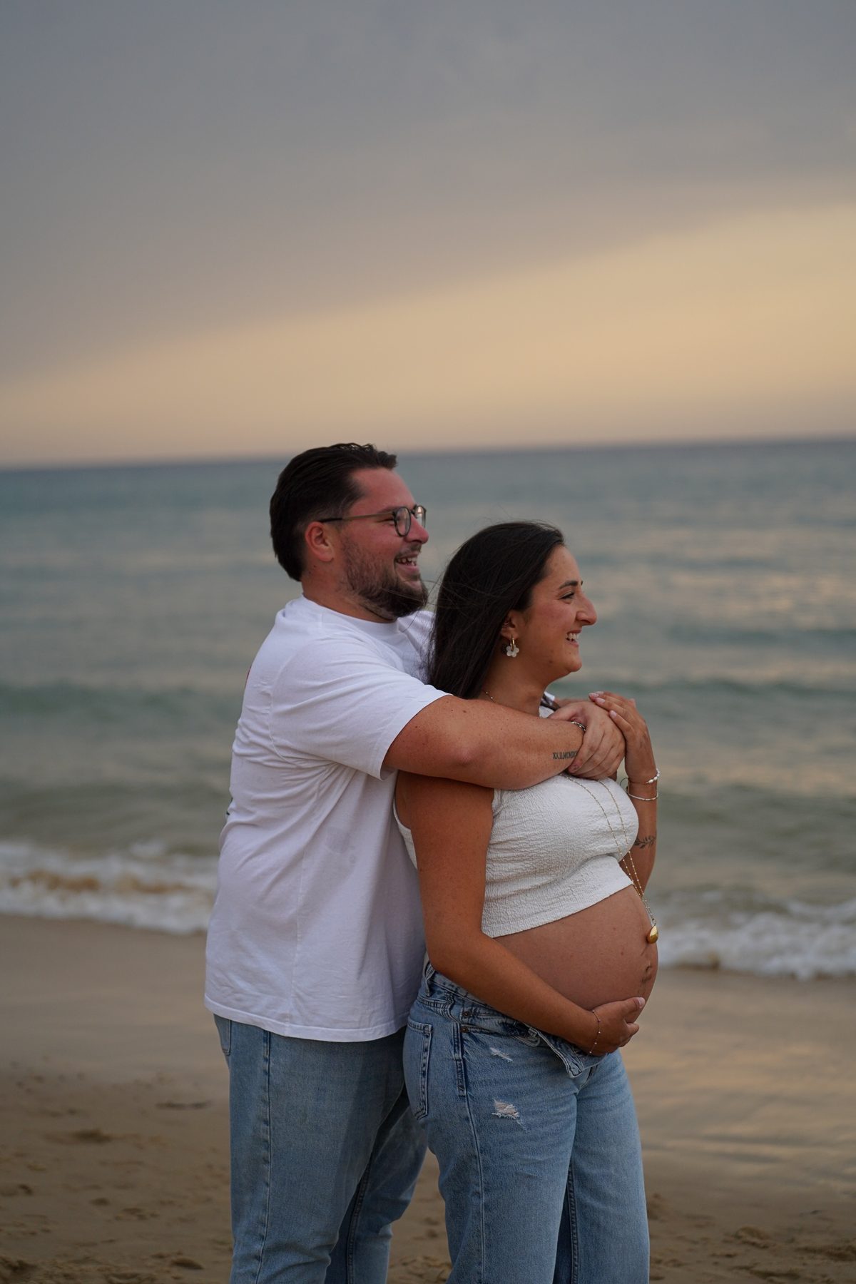 Shooting grossesse Noémie et Romain – Romain enlace Noémie devant la mer